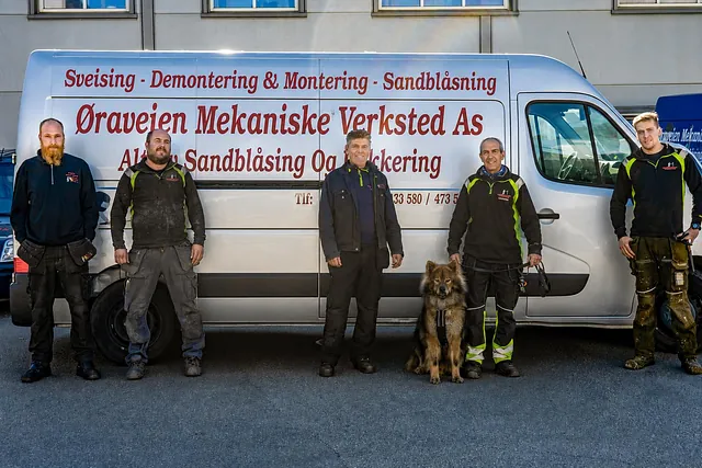Fem ansatte og en hund foran firmabilen til Øraveien Mekaniske Verksted AS